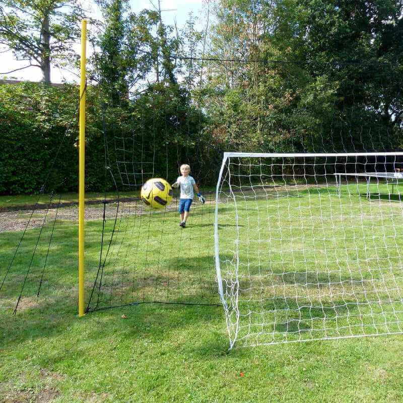 Junior playing with 3-in-1 soccer goal trainer and rebounder net in backyard