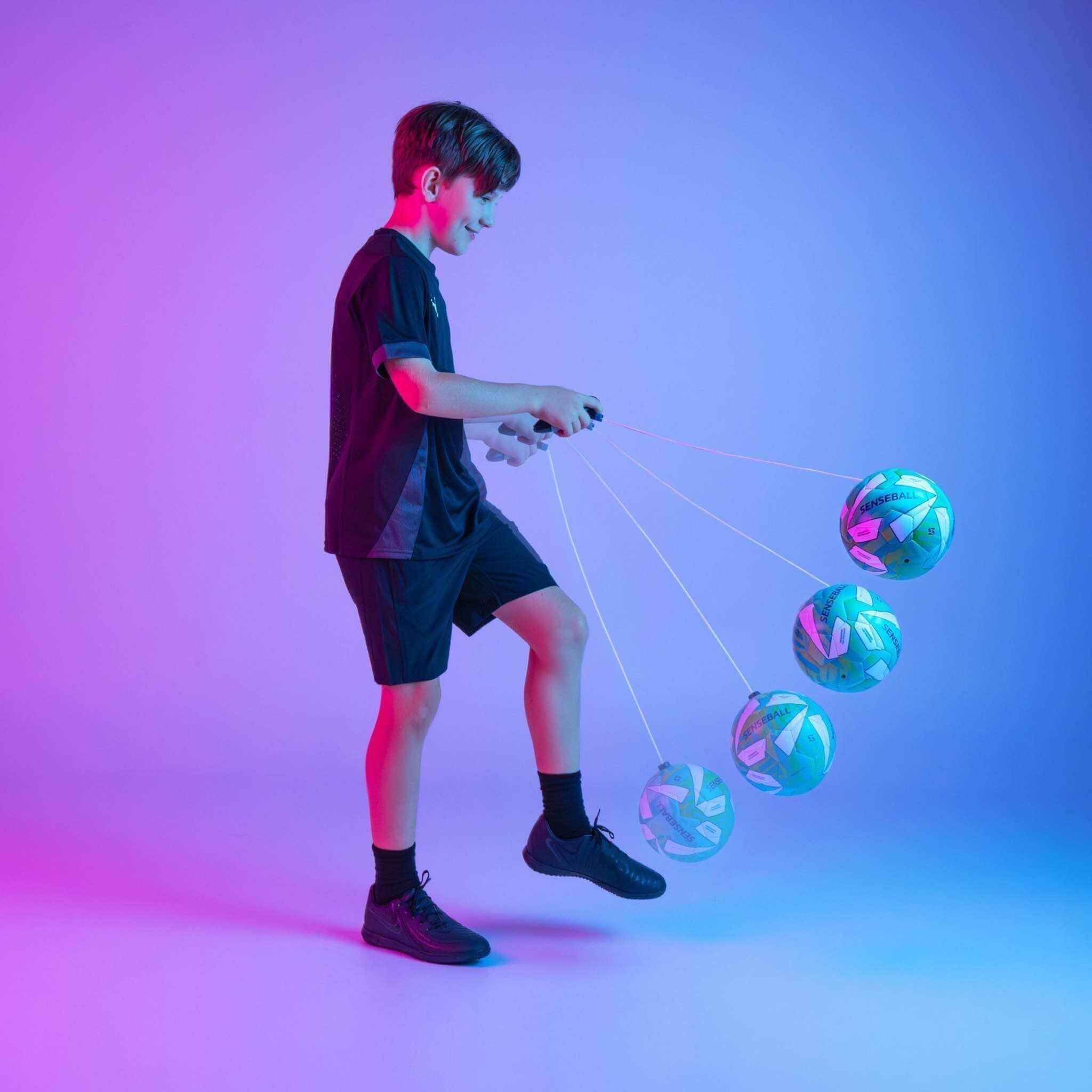Boy training soccer ball with SenseBall pro-level kick trainer on string in blue and purple light studio