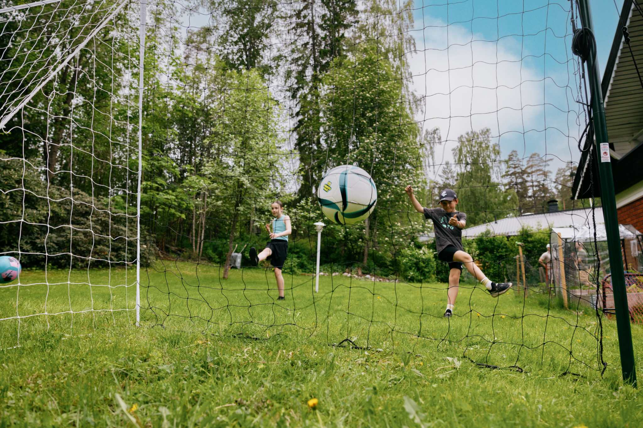 Kids practicing soccer with 3-in-1 soccer goal trainer in backyard