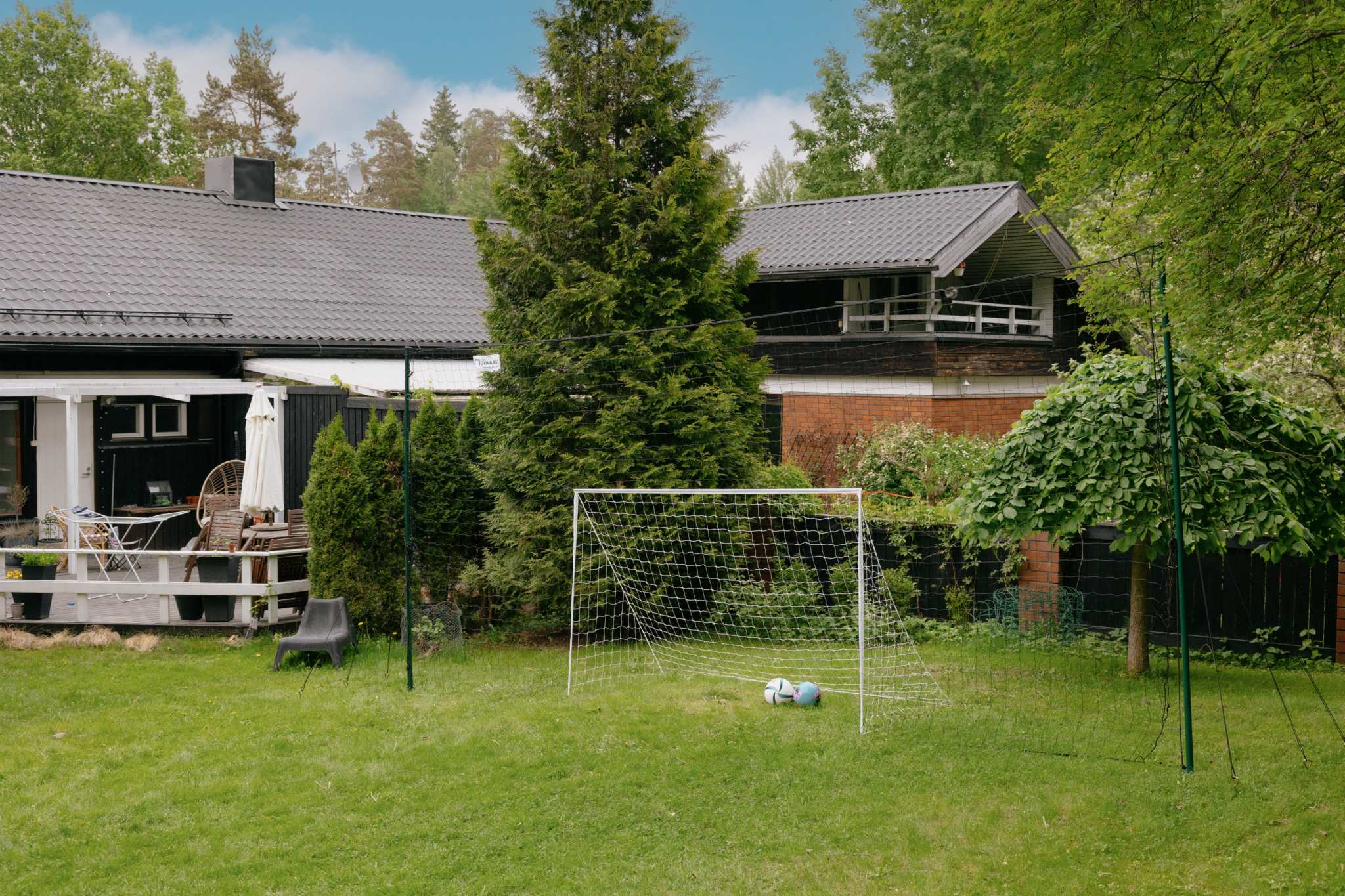 Standard-sized 3-in-1 soccer goal trainer set up in backyard with two soccer balls on grass