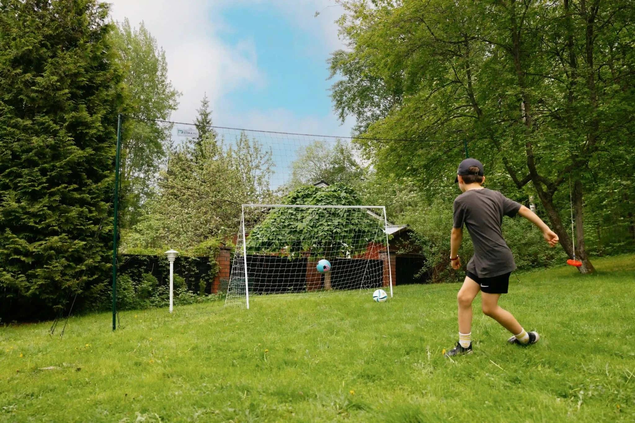 Child practicing with 3-in-1 soccer goal trainer in backyard.