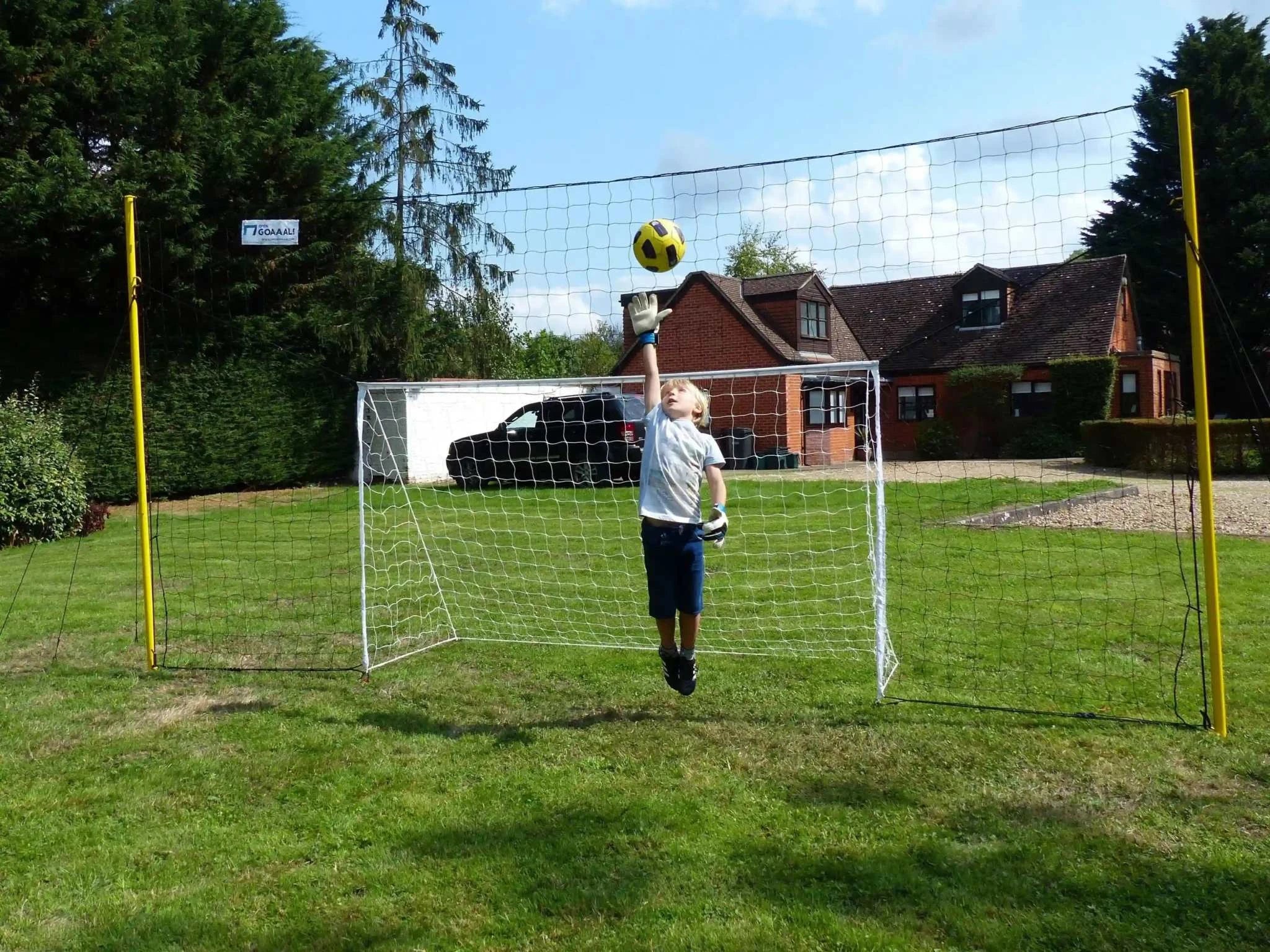 Open Goaaal® Soccer 3-in-1 Trainer in a garden setting with young player, featuring goal, rebounder, and backstop.
