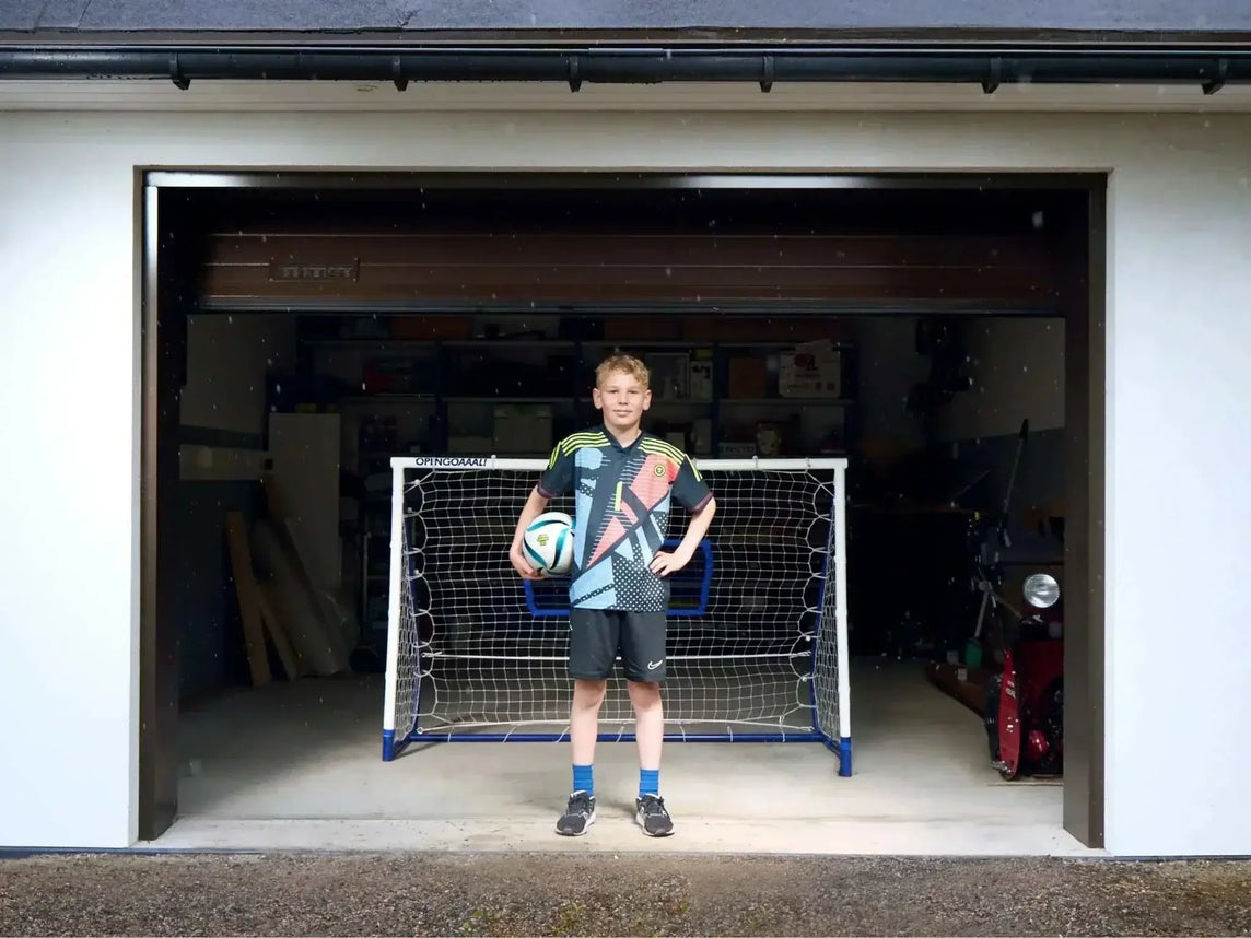 Boy standing with soccer ball in front of 3-in-1 soccer goal rebounder in garage doorway